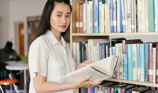 An Asian teenager reading a book in a college library, emphasizing education and learning.